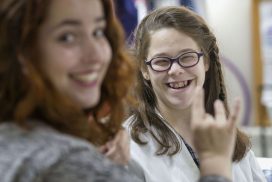 Alumna con necesidades especiales sonríe a la cámara mientras habla con su profesora en lengua de signos